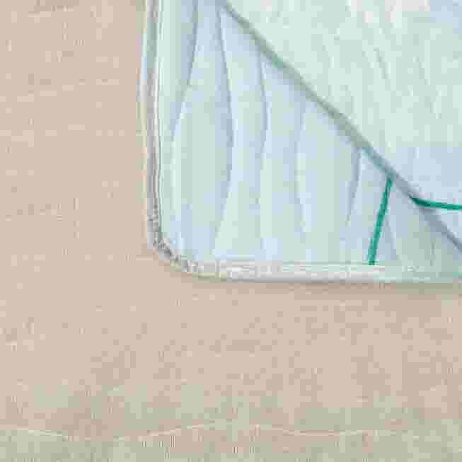 Corner of quilted sofa protector with light blue fabric and green trim