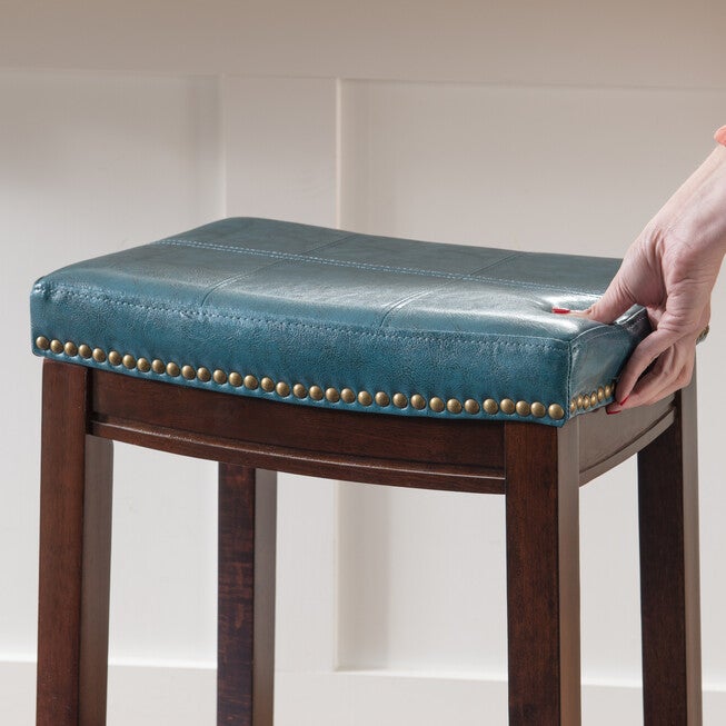 Claridge faux leather bar stool with teal seat and nailhead trim being adjusted