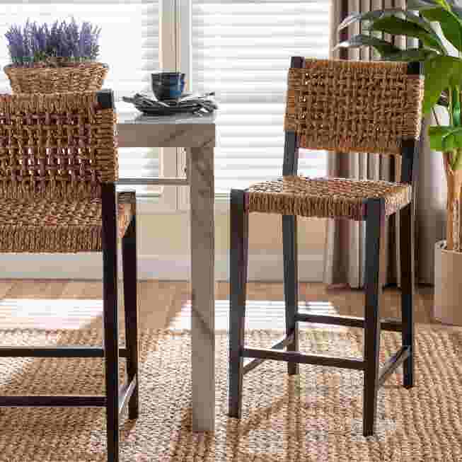 Two seagrass bar stools with black frames in a dining area.